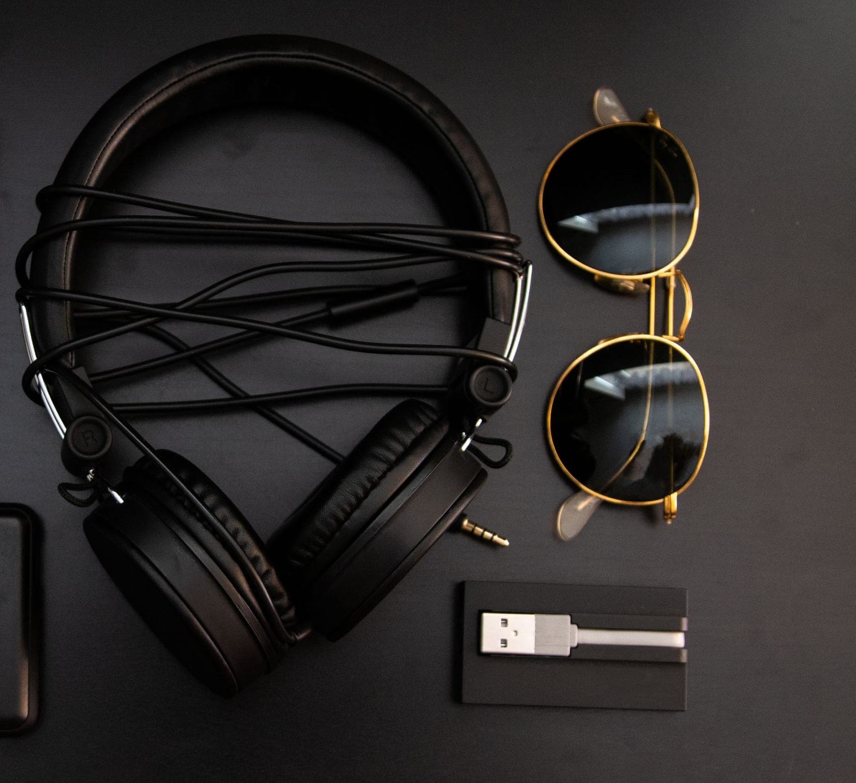 Black over-ear headphones with a cable, next to a pair of sunglasses