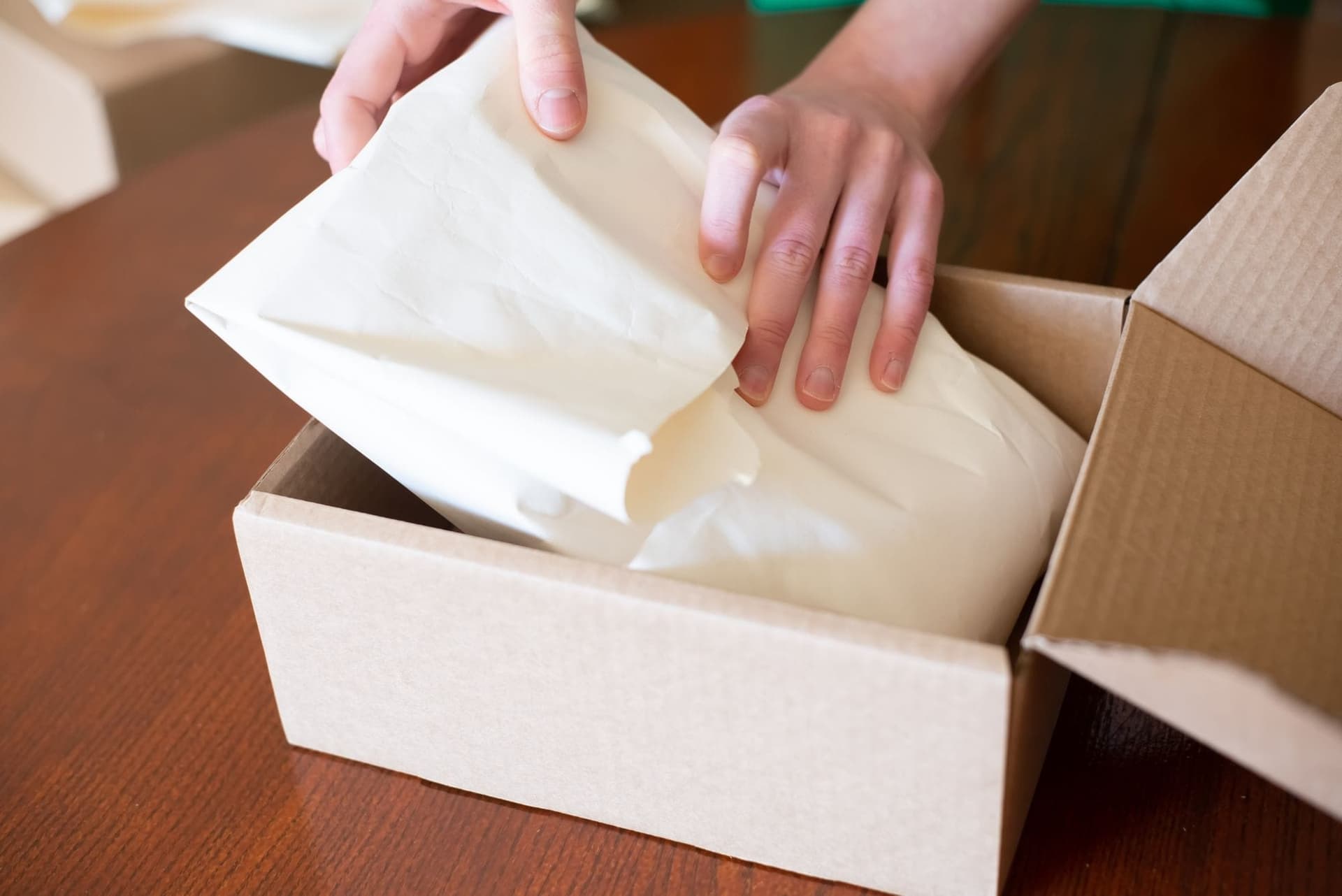 Hands packing an order into a cardboard box with tissue paper